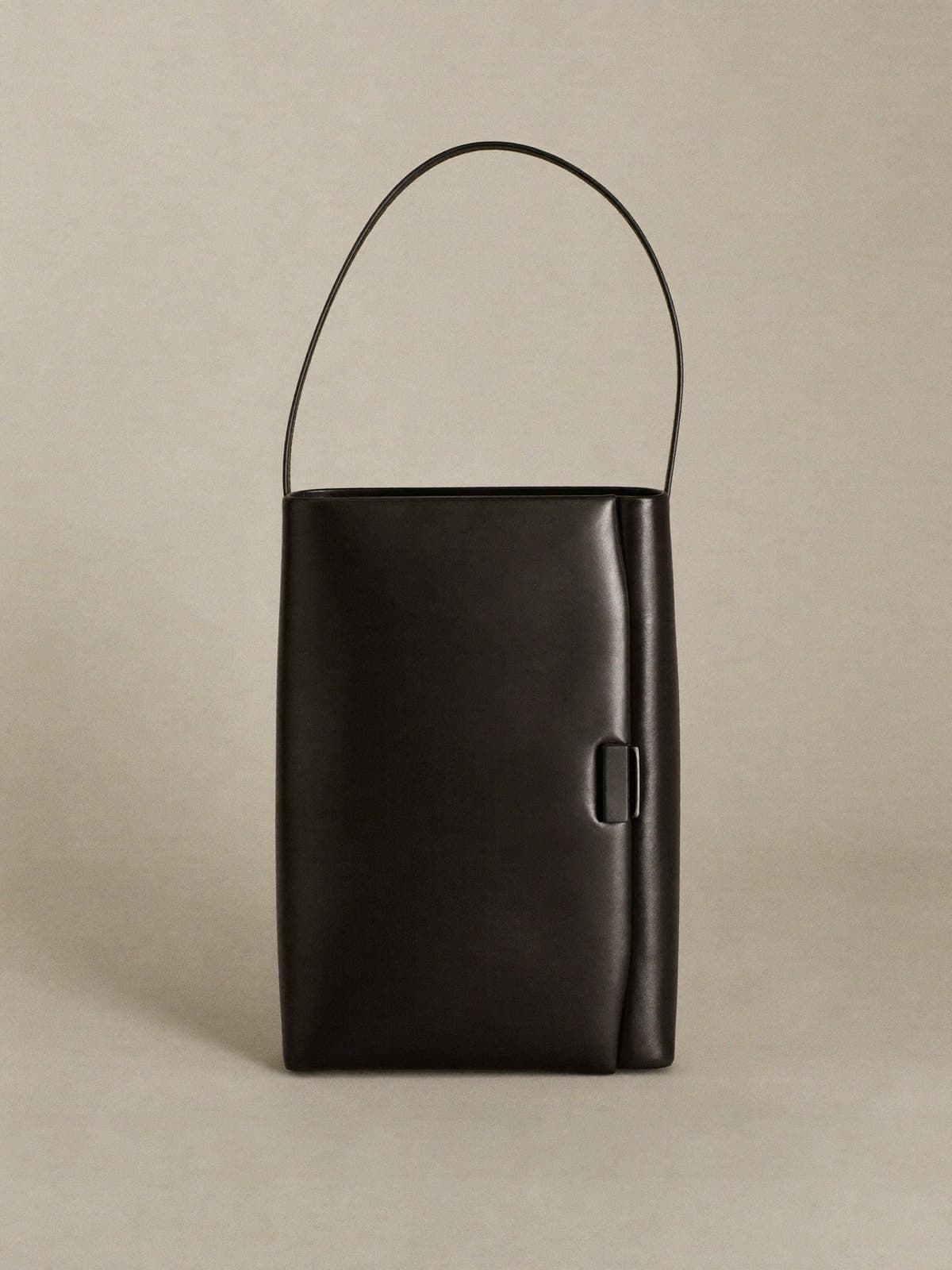 A minimal black leather shoulder bag on light grey paper.