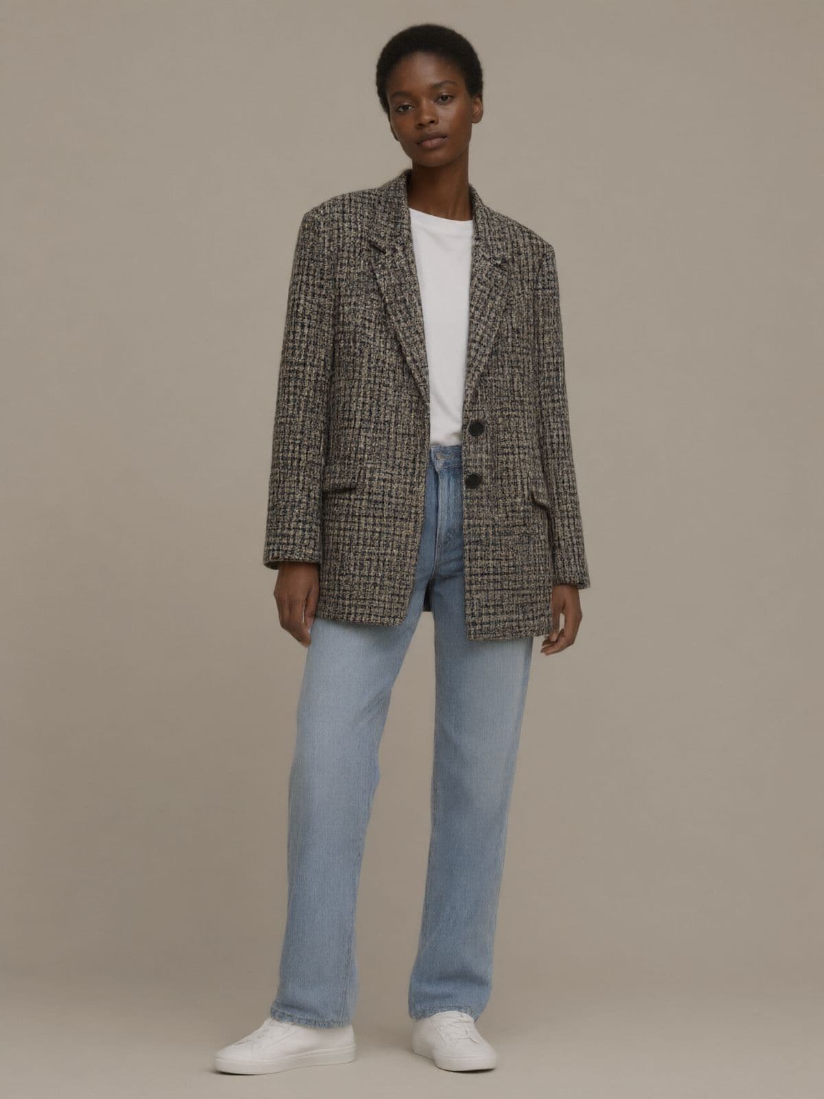 A woman wears the check blazer open over a white T-shirt, light blue jeans and white sneakers.