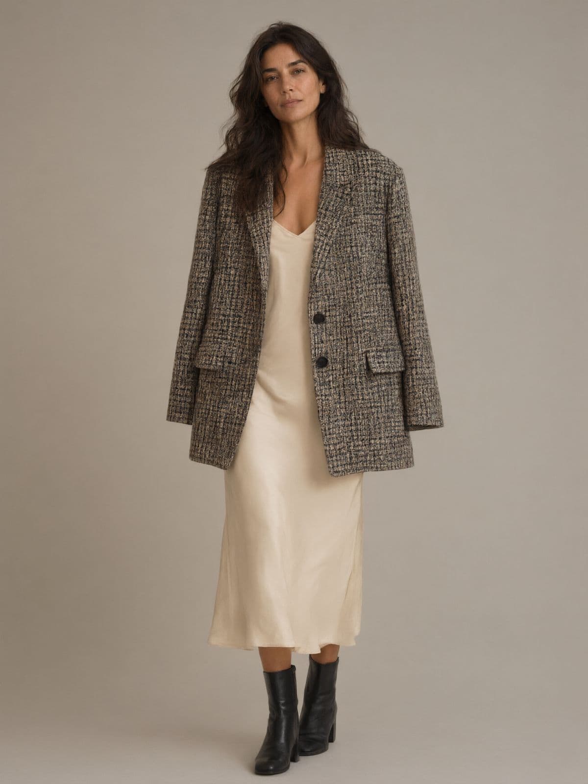 A woman wears the check blazer over a cream silk slip dress with black ankle boots.