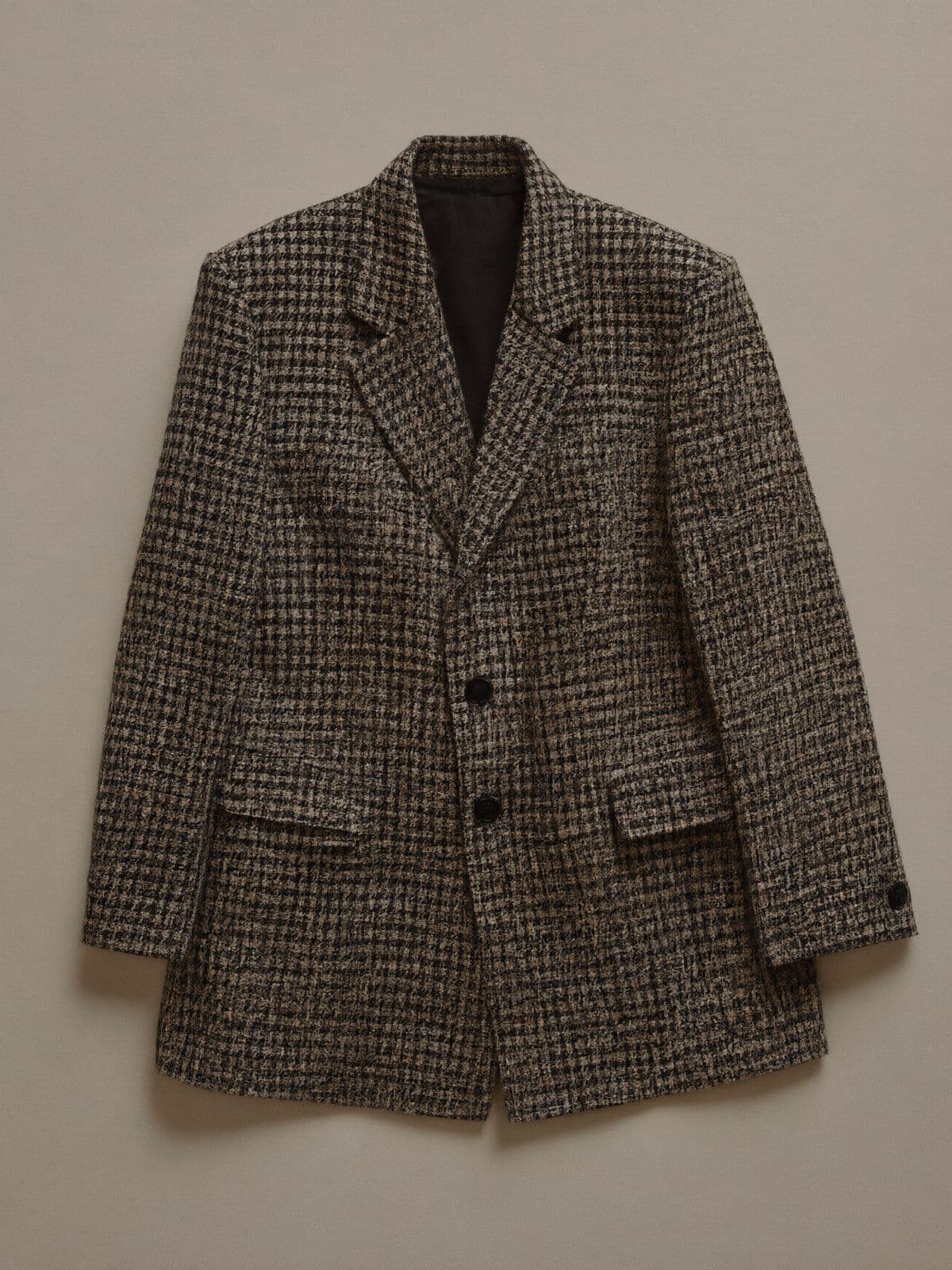 A black and ivory check wool blazer laid flat on light grey paper.
