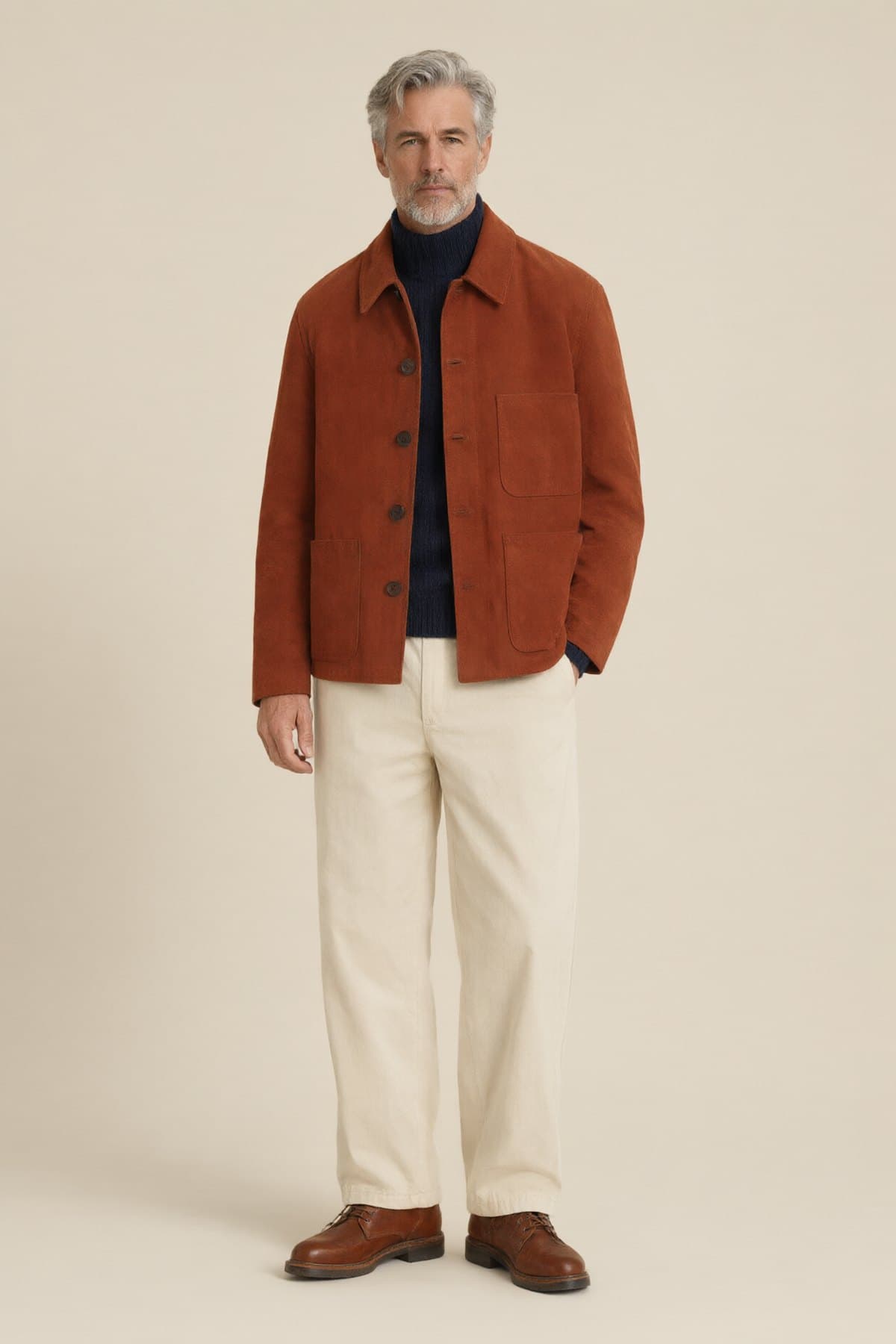 A man wears the rust suede jacket over a navy rollneck with ecru chinos and brown boots.