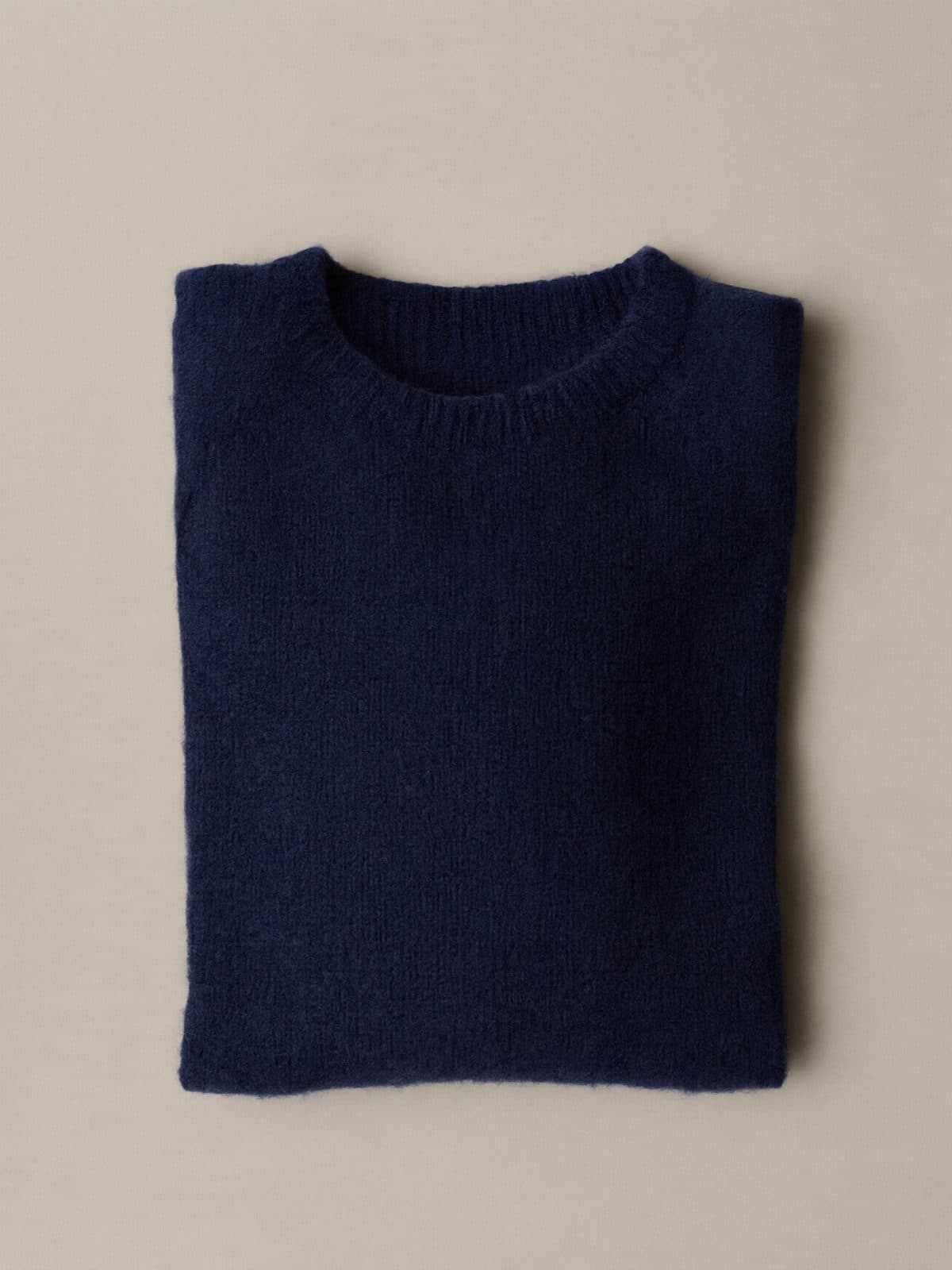 A folded navy crew-neck wool sweater on light grey paper.