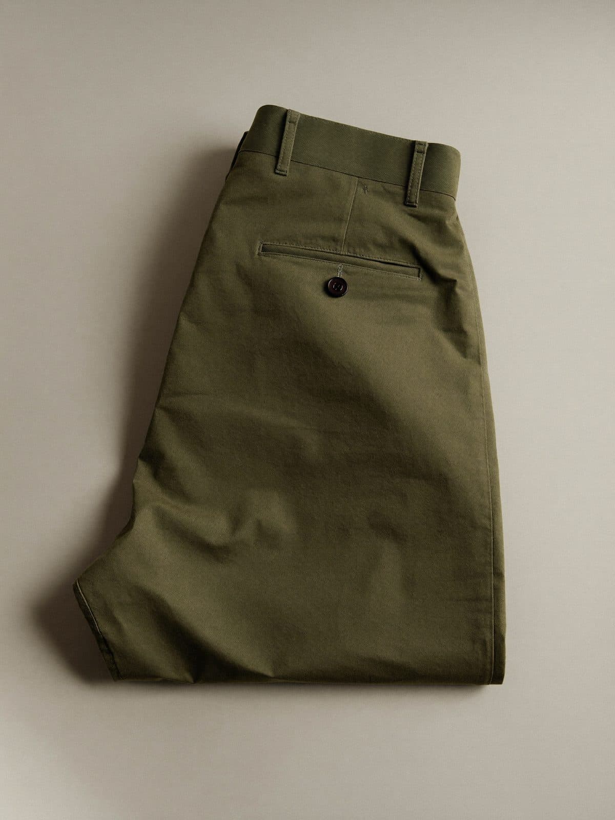 Folded olive green cotton trousers on light grey paper.