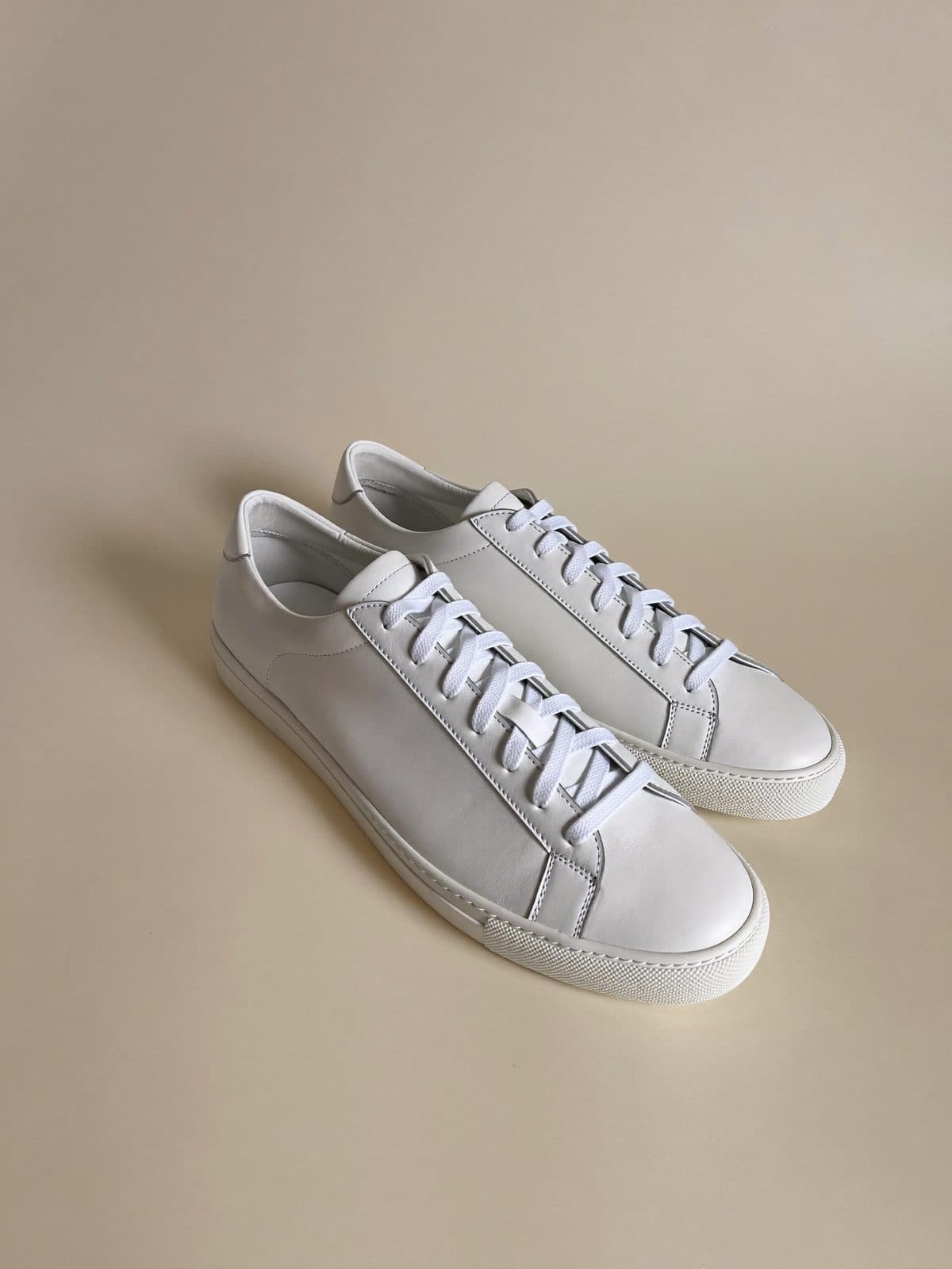 A pair of minimal white leather sneakers on light grey paper.